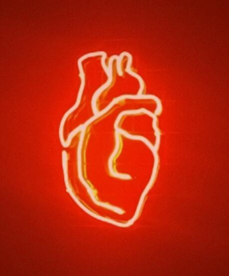 A vivid red neon heart glowing in a dark futuristic space with reflective surfaces.