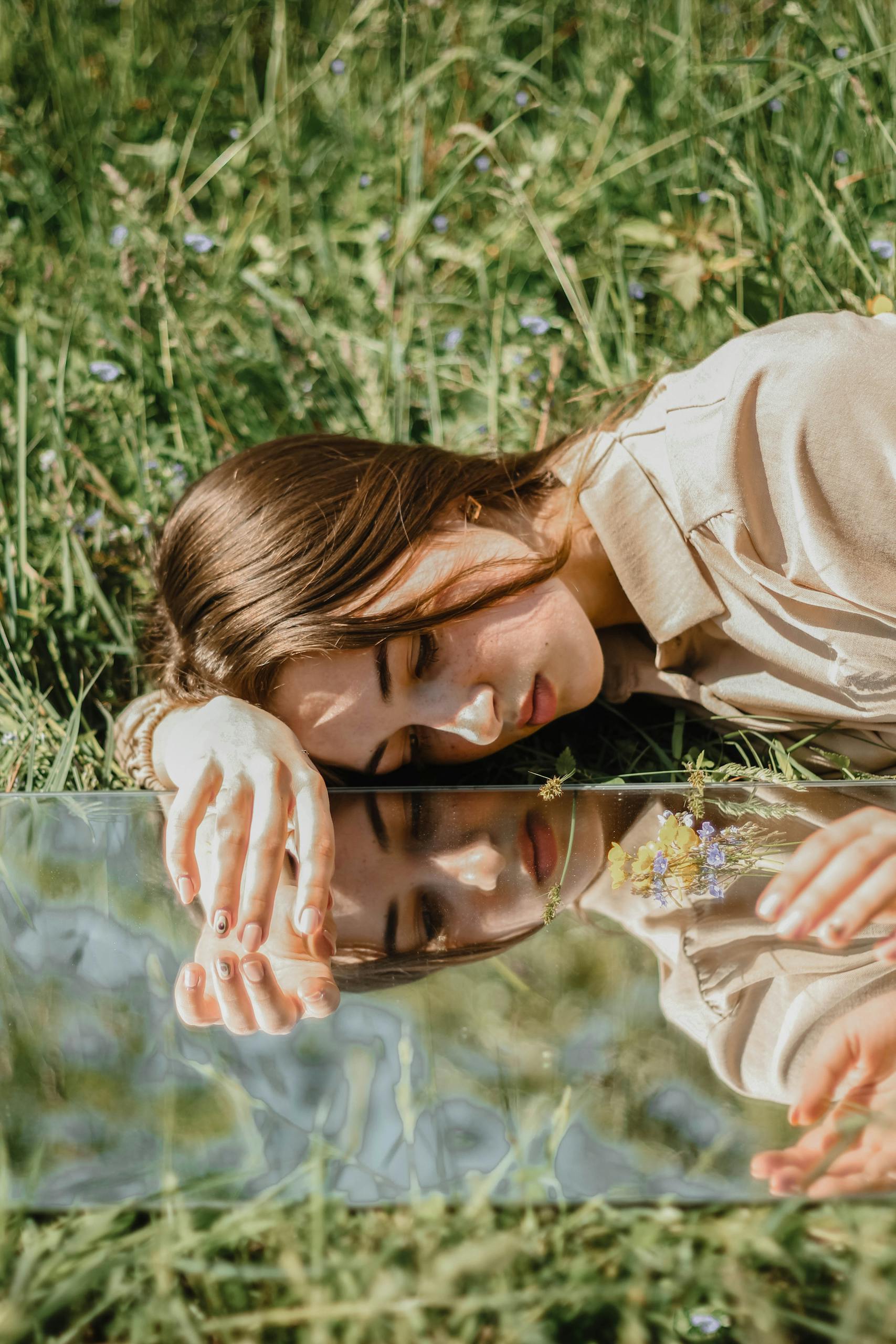 Portrait of a woman lying on grass, reflecting on a mirror, depicting contemplation and serenity.
