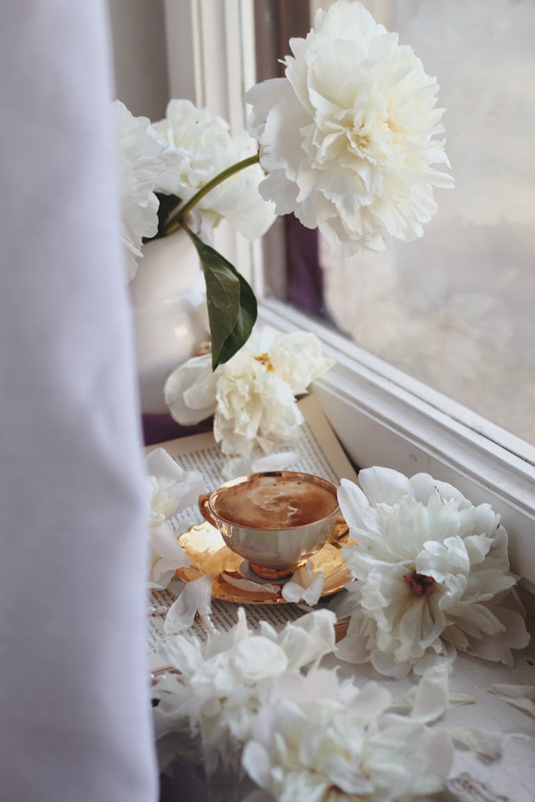Relaxing coffee break with white peonies on a windowsill, creating a serene atmosphere.