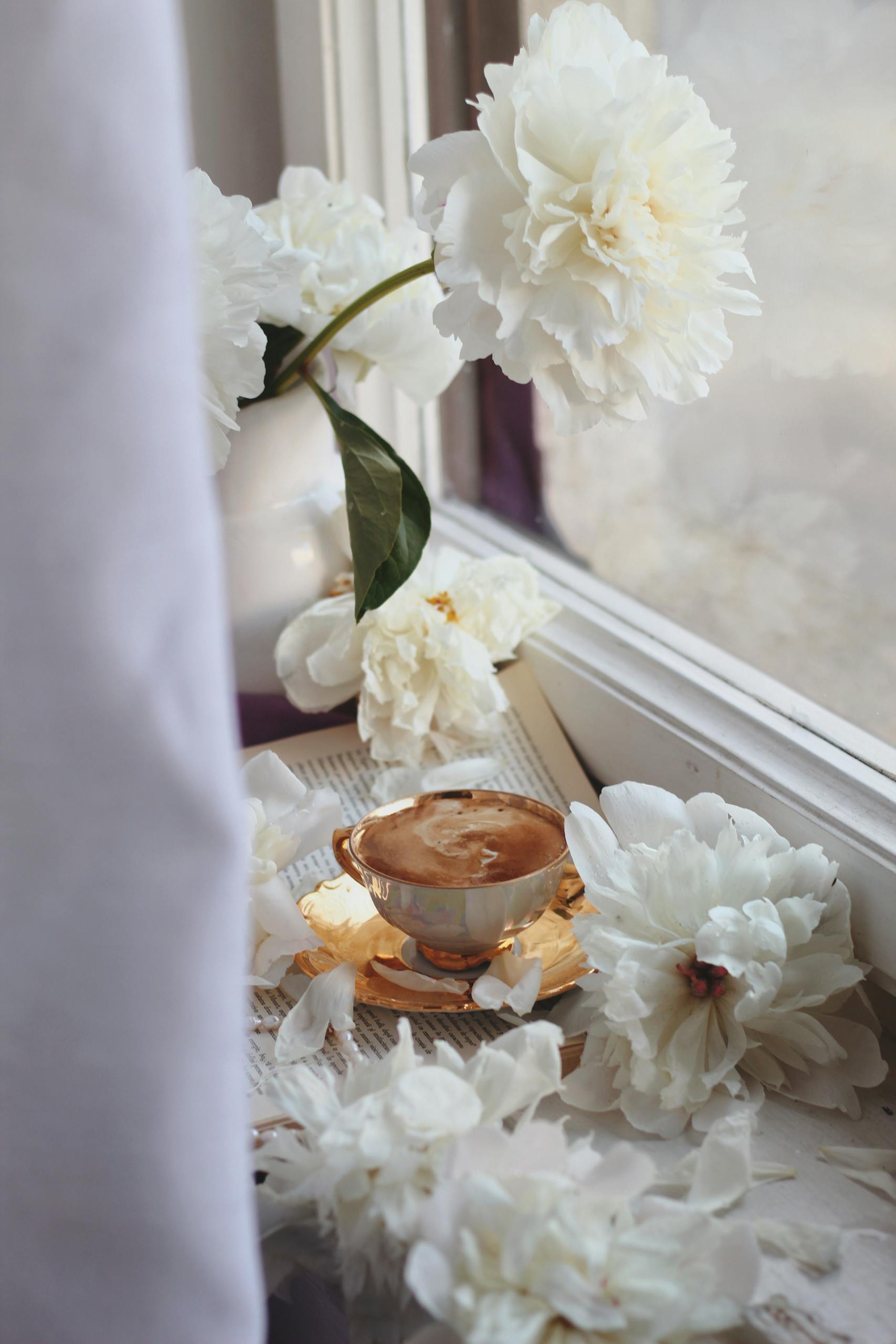 Relaxing coffee break with white peonies on a windowsill, creating a serene atmosphere.