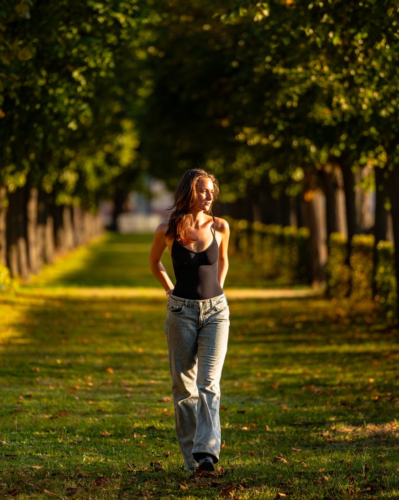 Serene scene of a woman walking on a sunny park pathway surrounded by trees.