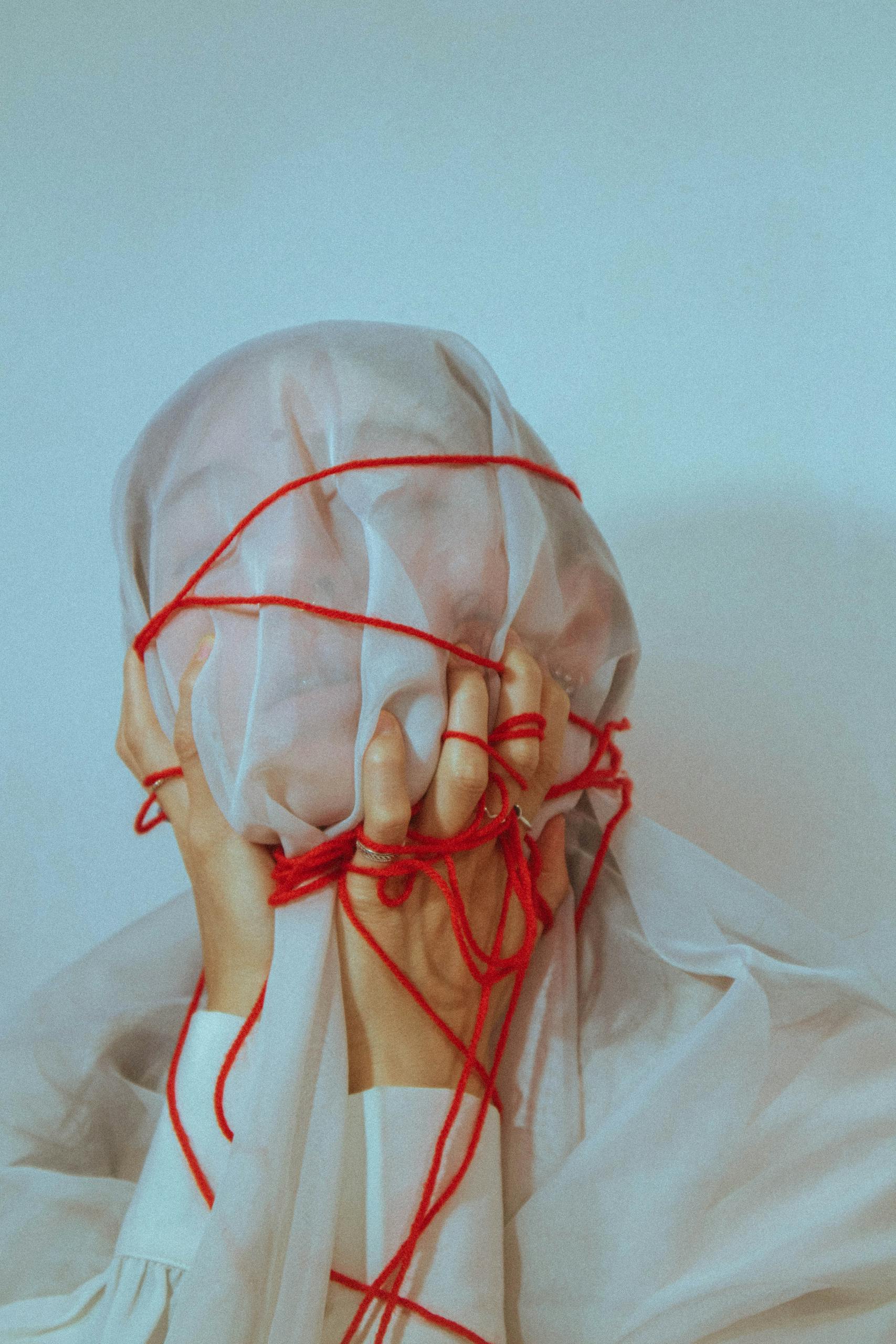 Surreal portrait of a covered face wrapped with red yarn creating a conceptual art piece.