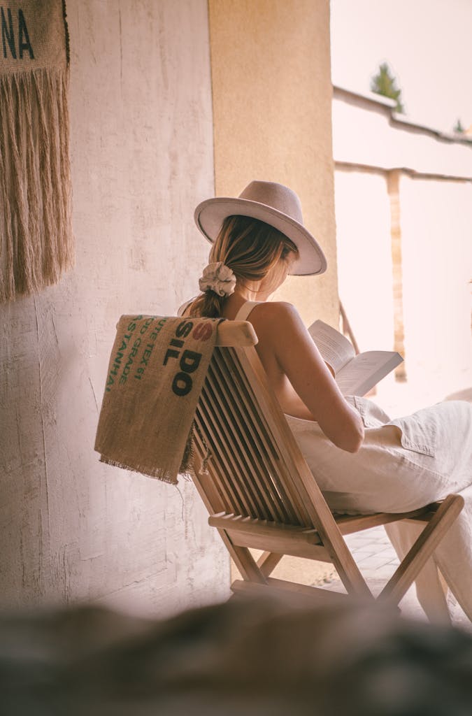Woman in hat reading a book outdoors, embodying relaxation and leisure.