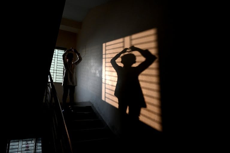 A person creates a silhouette on a stairway with dramatic shadows from a window.