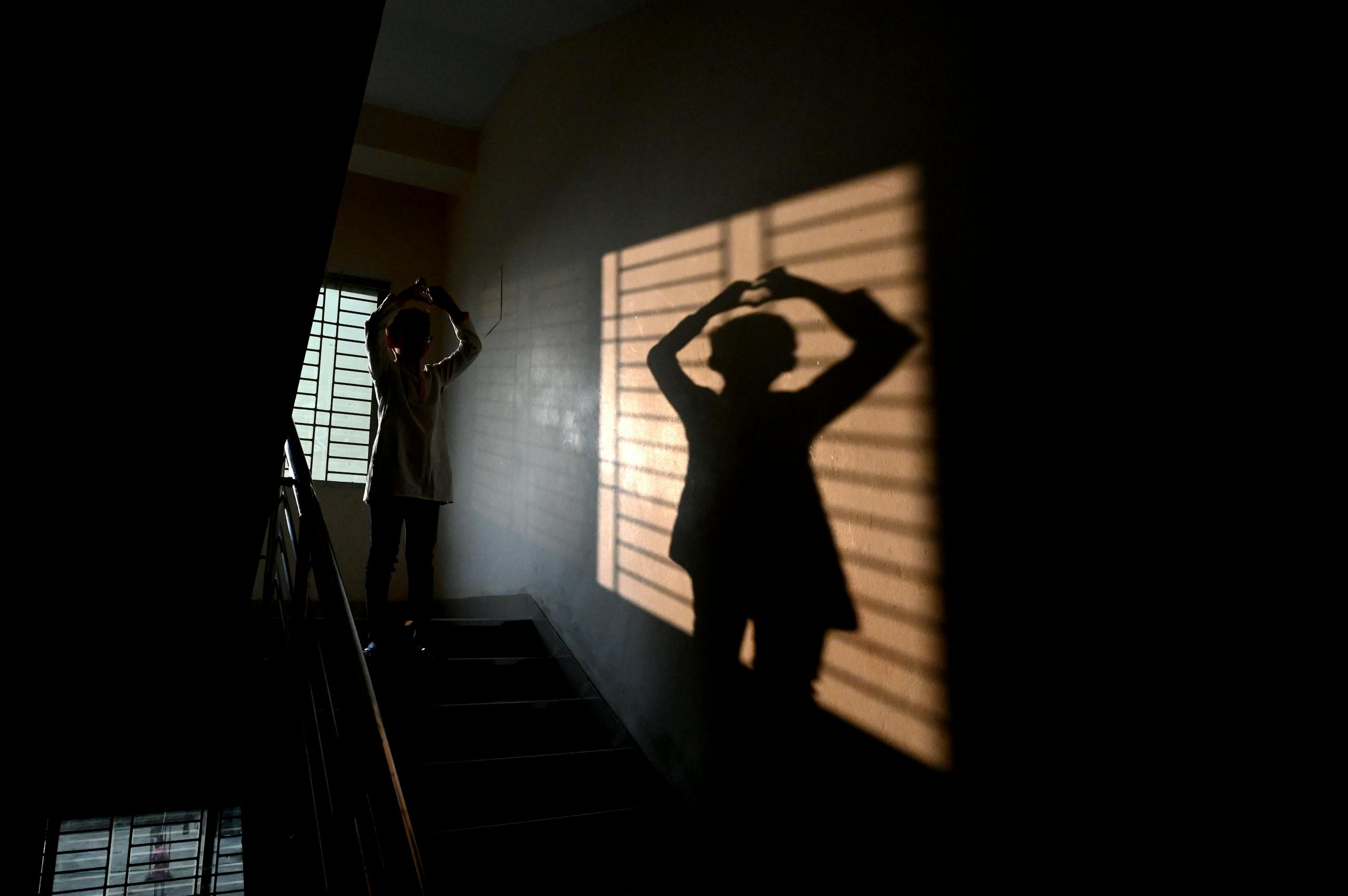 A person creates a silhouette on a stairway with dramatic shadows from a window.