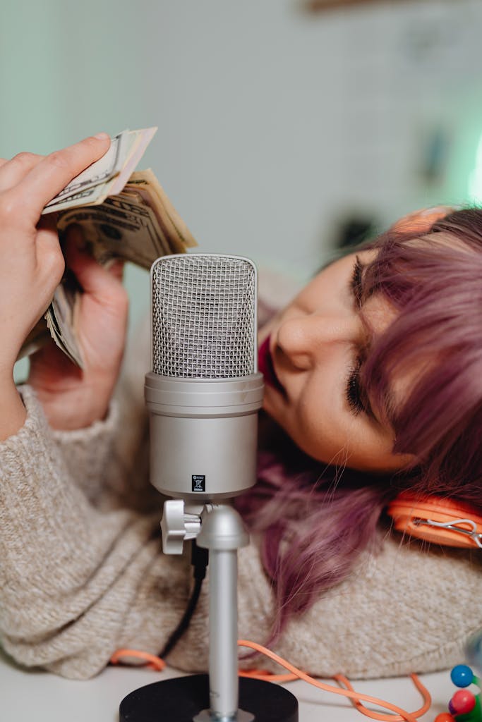 Young woman counts cash while holding a microphone for ASMR recording.