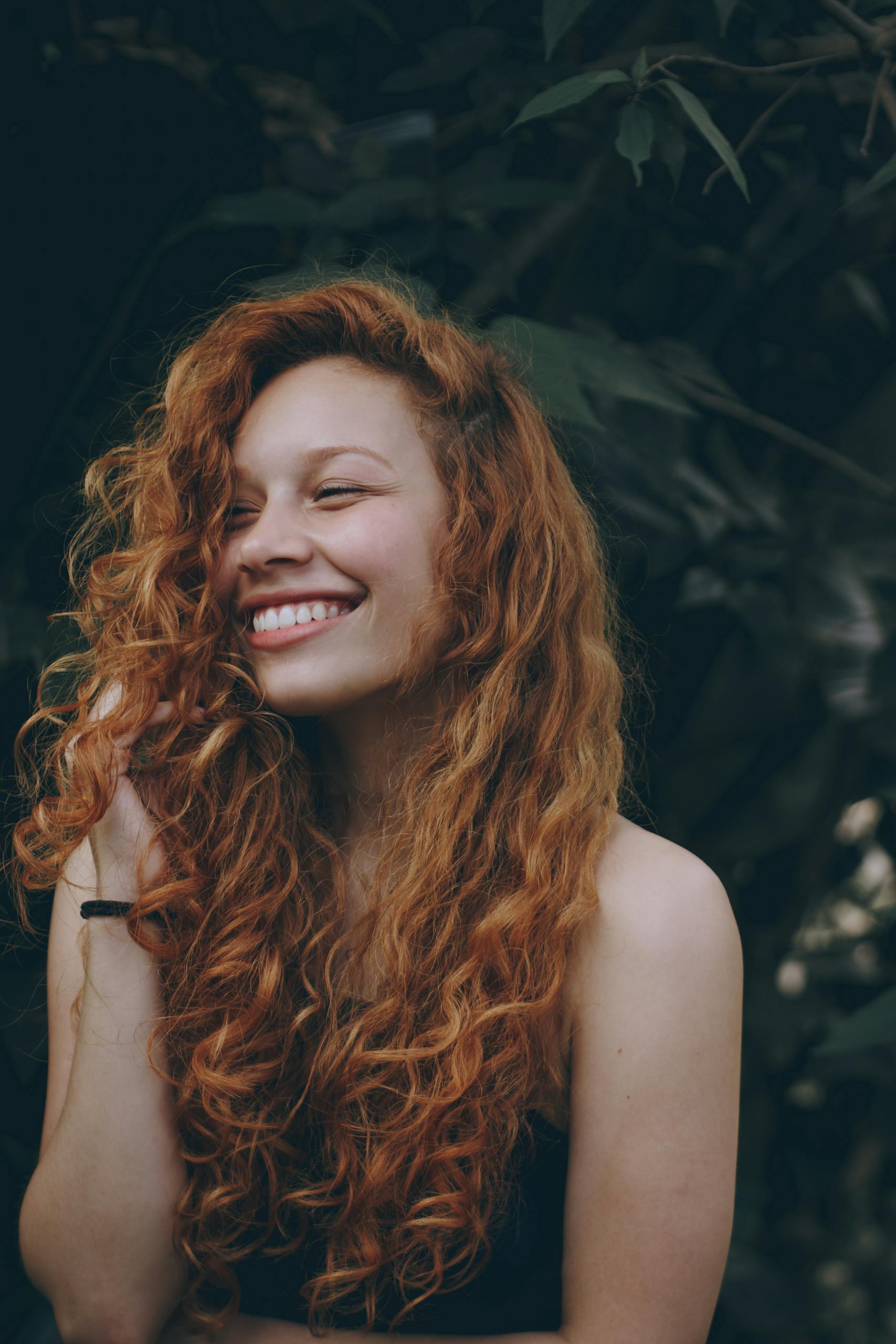 A candid portrait of a joyful woman with curly red hair, expressing natural beauty and happiness.